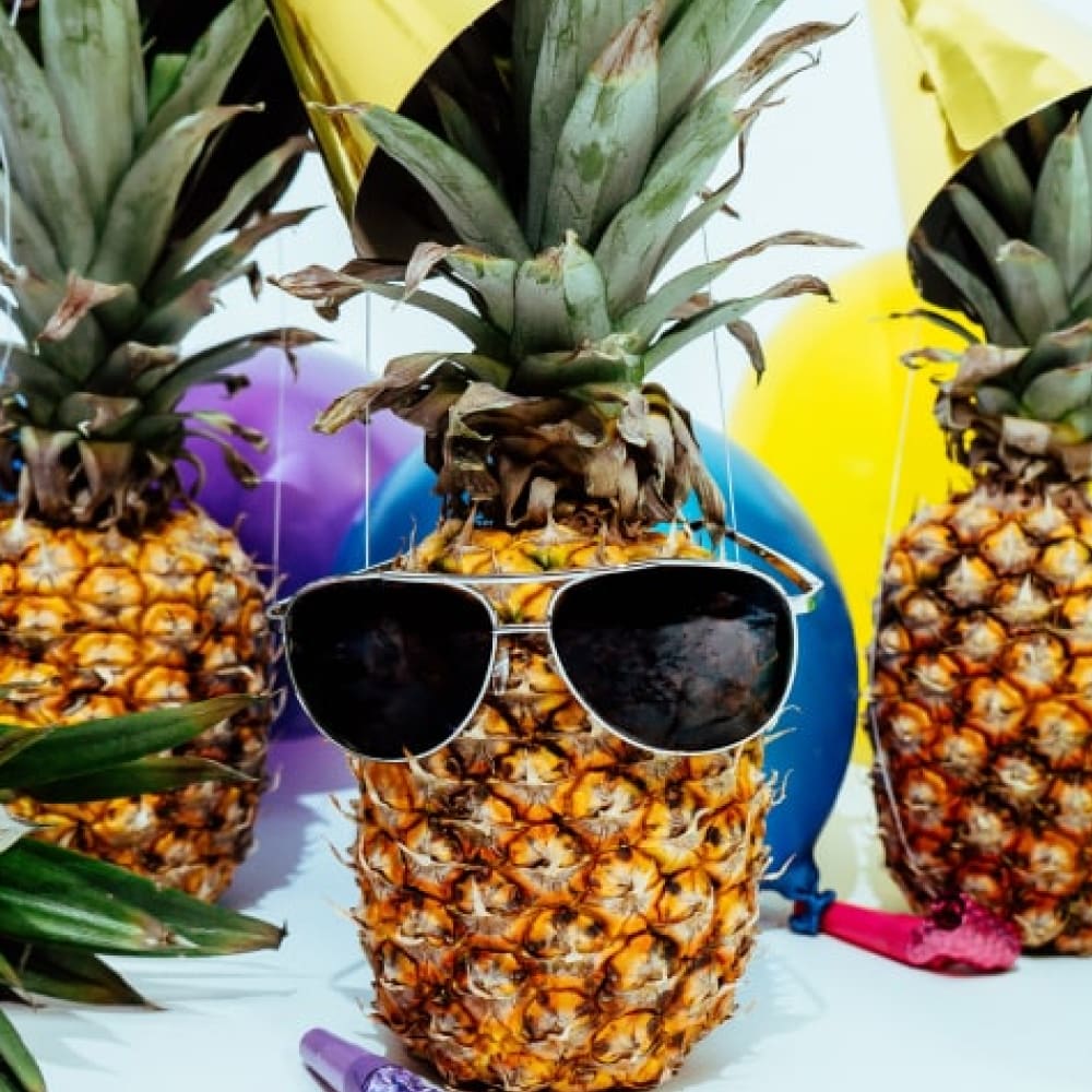 Three pineapples. The center pineapple is wearing aviator sunglasses.
